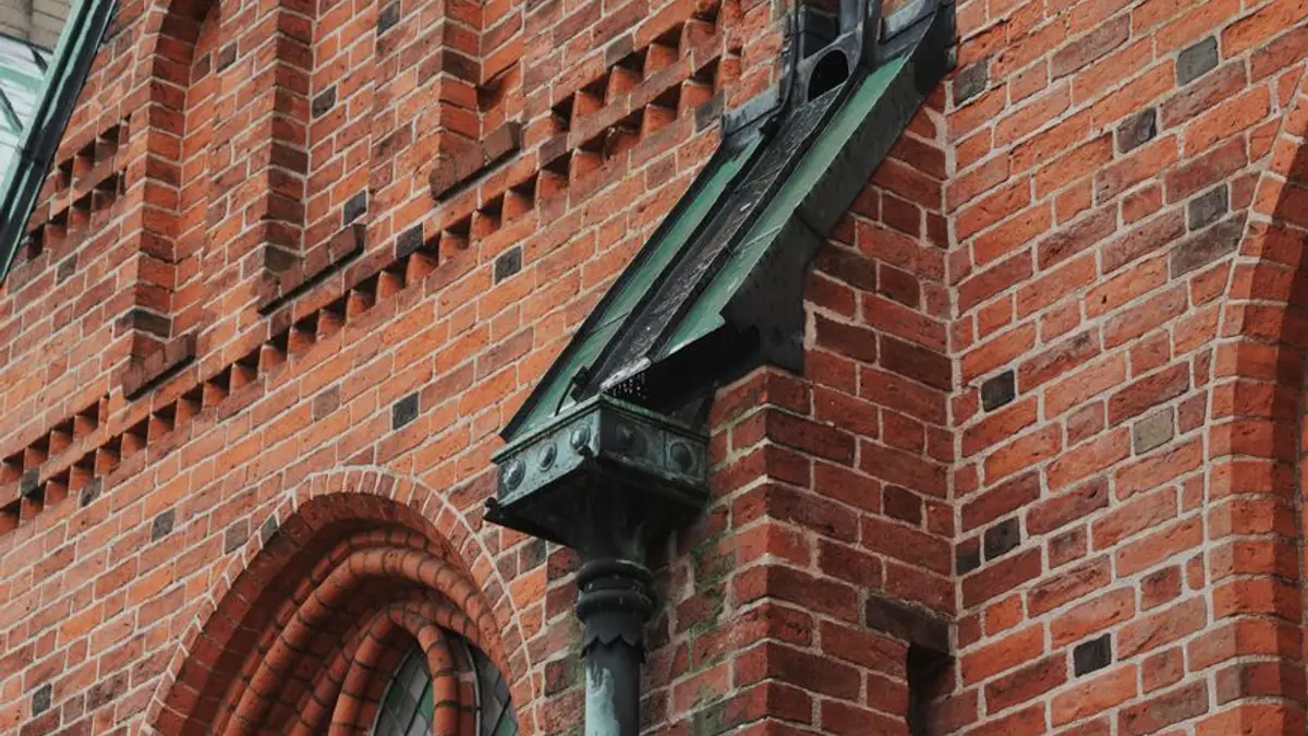 Weathered copper downspout head on a red brick wall