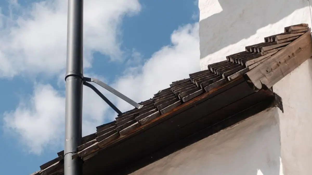 Tile roof edge with a round downspout and bracket against a blue sky