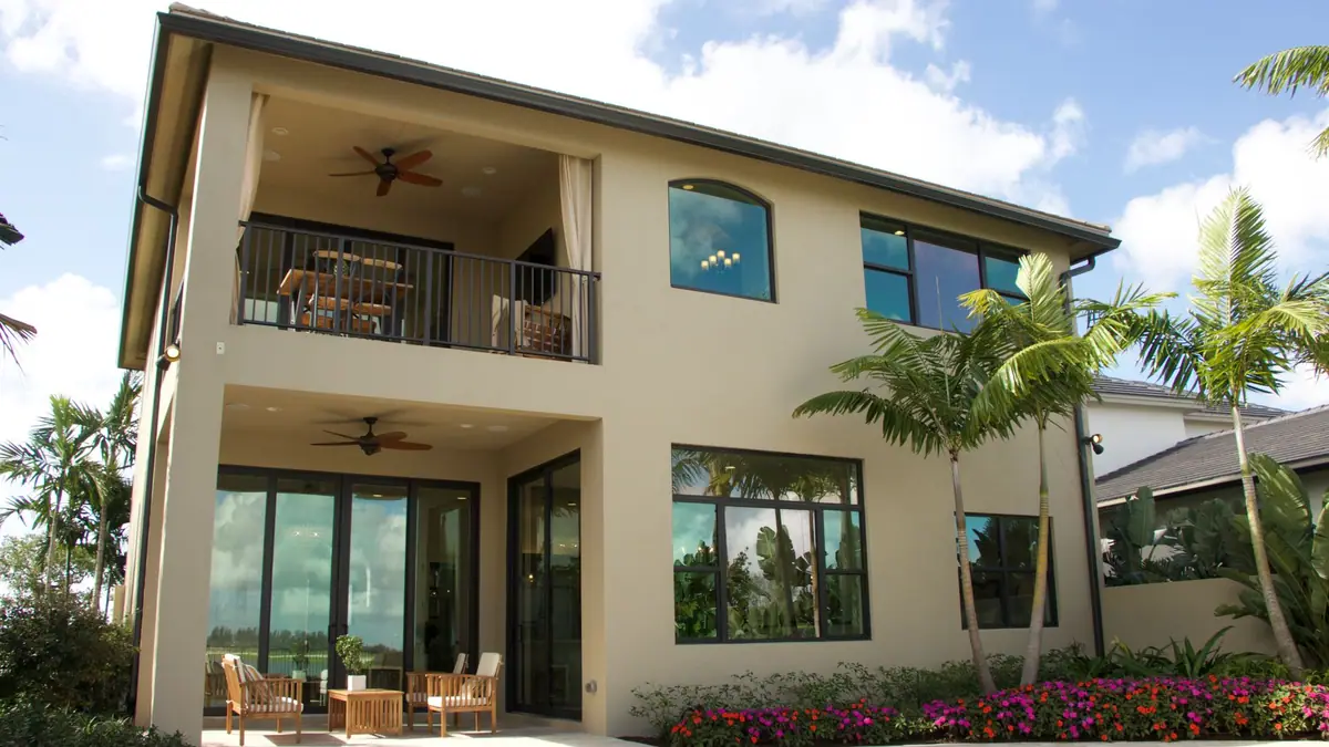 Two-story stucco home with a covered balcony, palms, and flowers