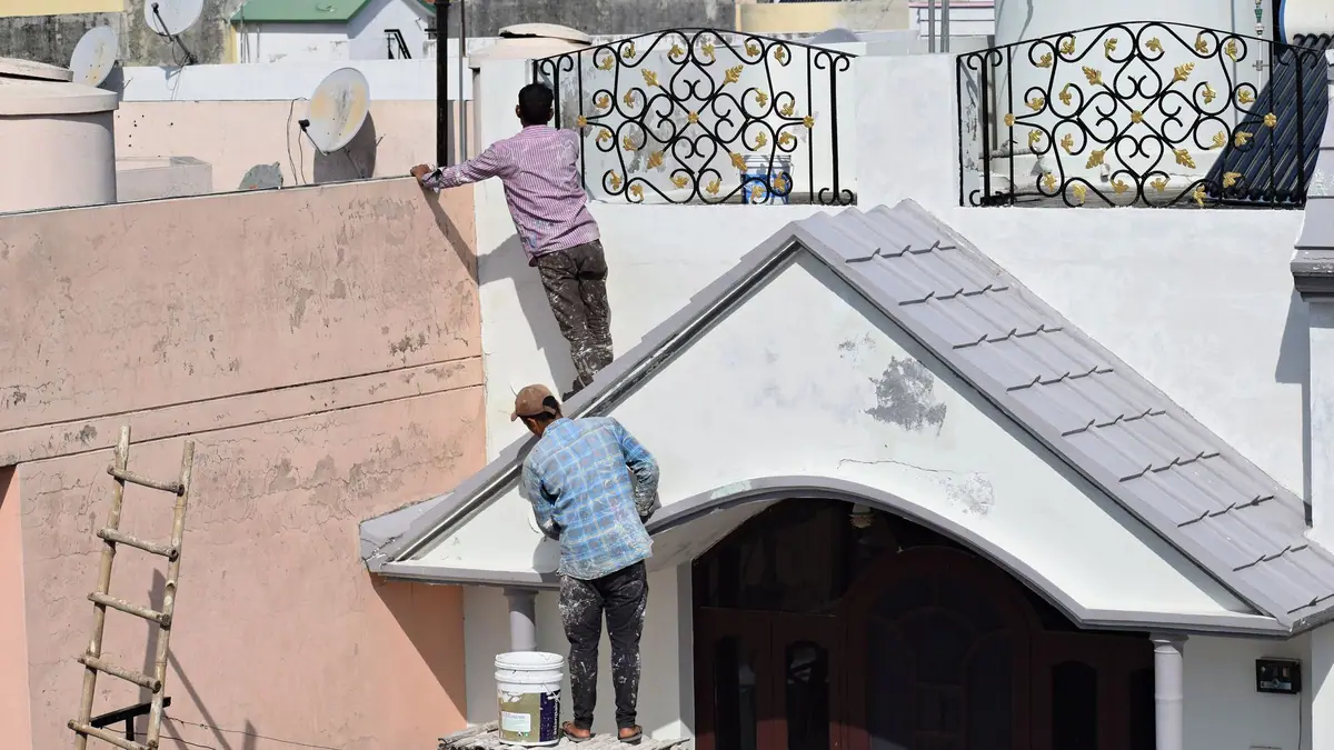 Workers repairing the exterior of a stucco house with a ladder against the wall