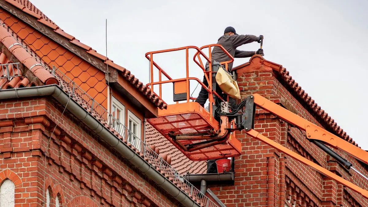 Worker on a lift replacing gutters along a tile and brick roofline