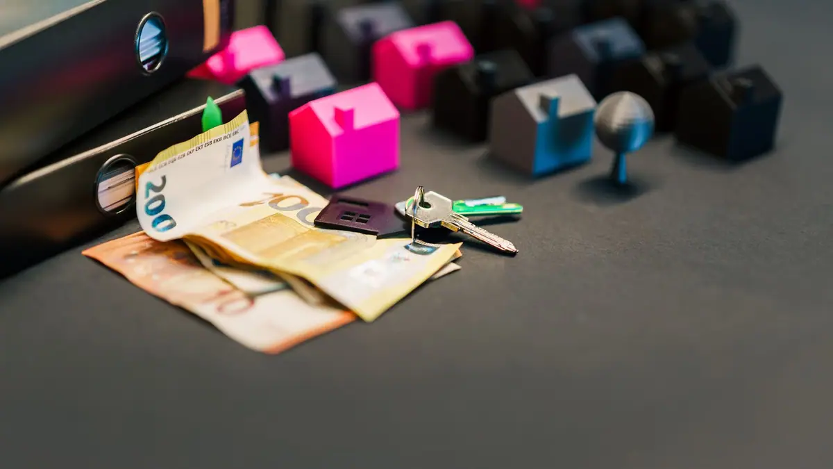 Small model houses, house keys, and cash on a dark surface