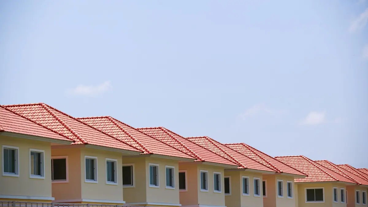 Row of stucco townhomes with red tile roofs under a blue sky