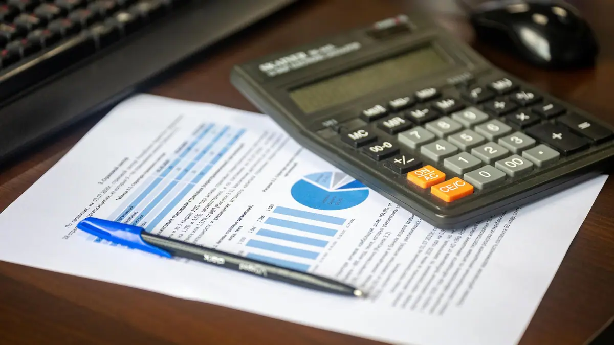 Calculator and printed cost charts on a desk with a pen