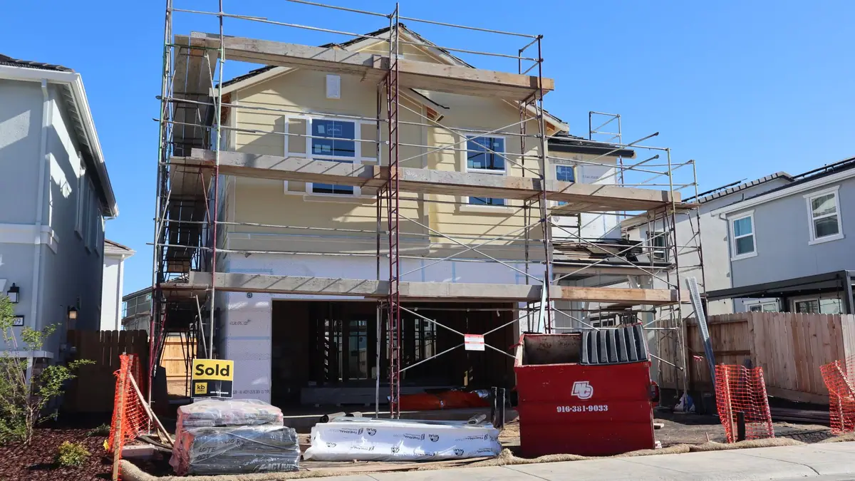 New home under construction with scaffolding and a dumpster out front