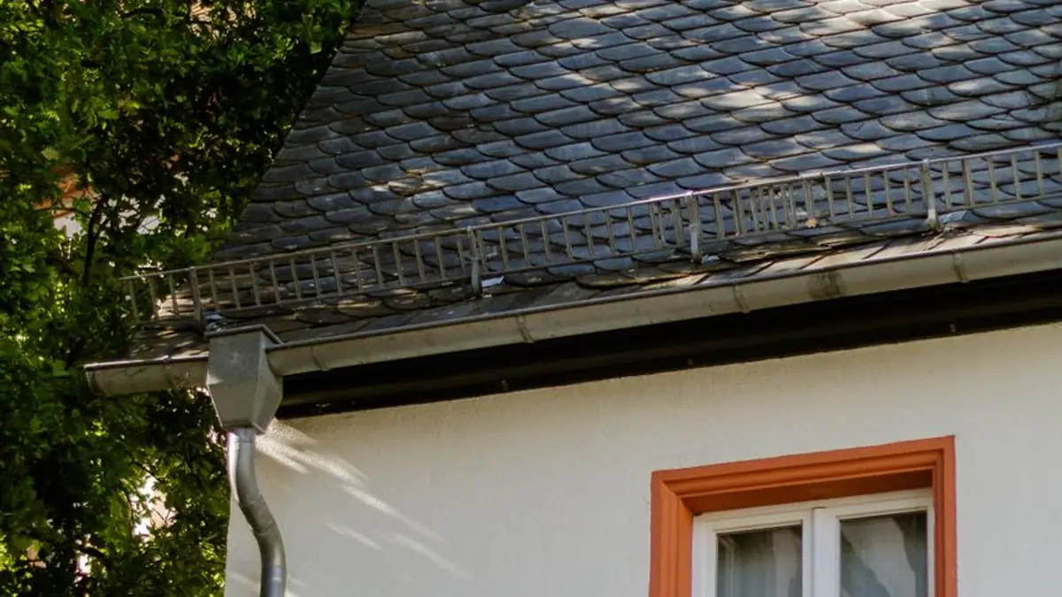 White house with a slate roof, a gutter, and a downspout beside an orange window frame