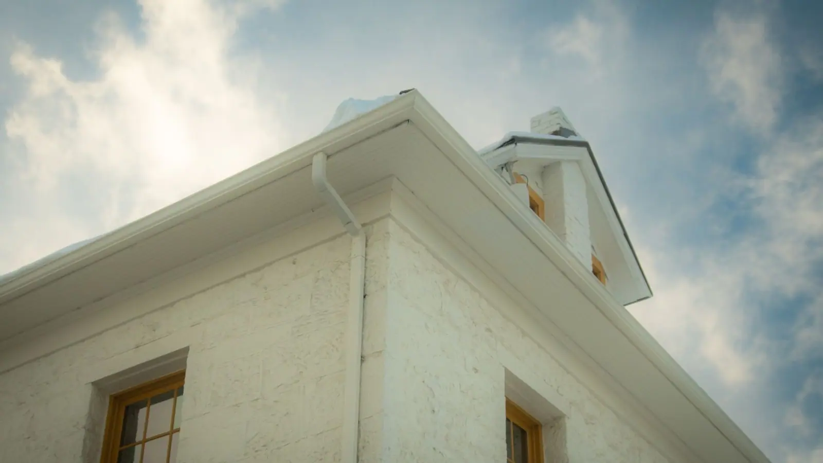 White gutter and downspout on the corner of a white house under a blue sky