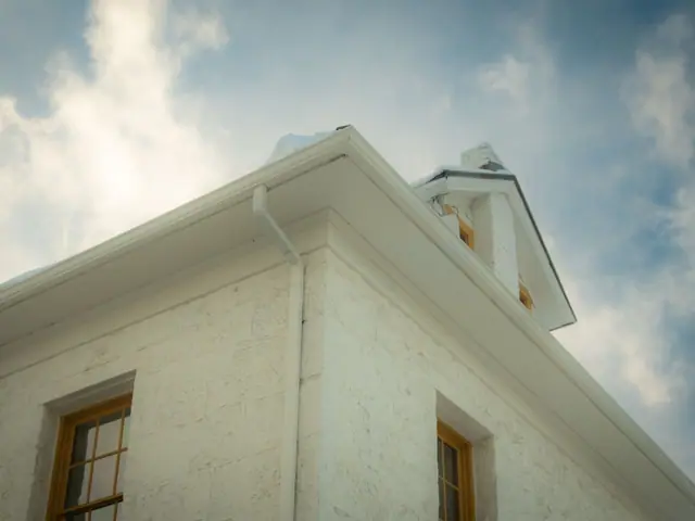 White gutter and downspout on the corner of a white house under a blue sky