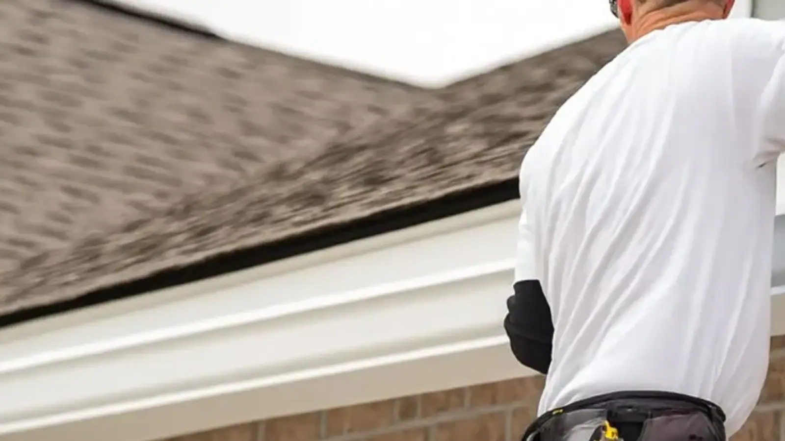 Person on a telescoping ladder reaching into a roof gutter to clear it