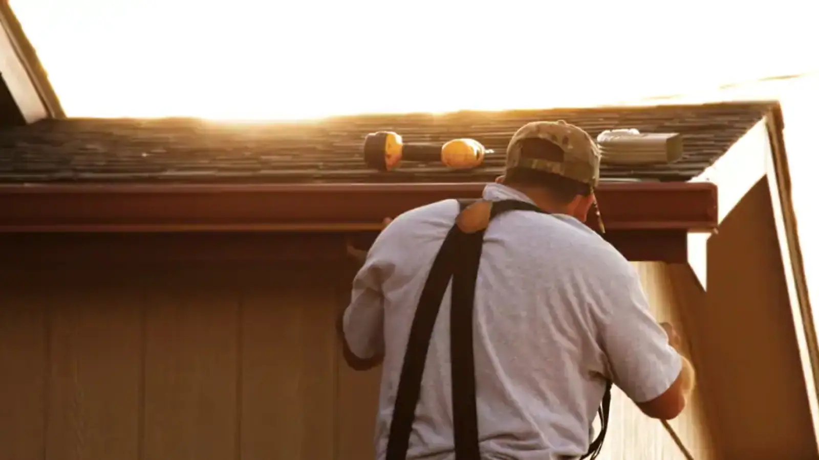 Installer working on a gutter at the roof edge in late-afternoon sun