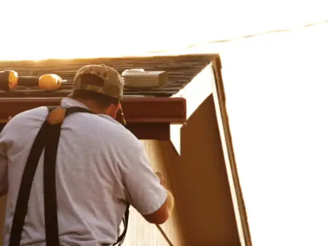 Installer working on a gutter at the roof edge in late-afternoon sun