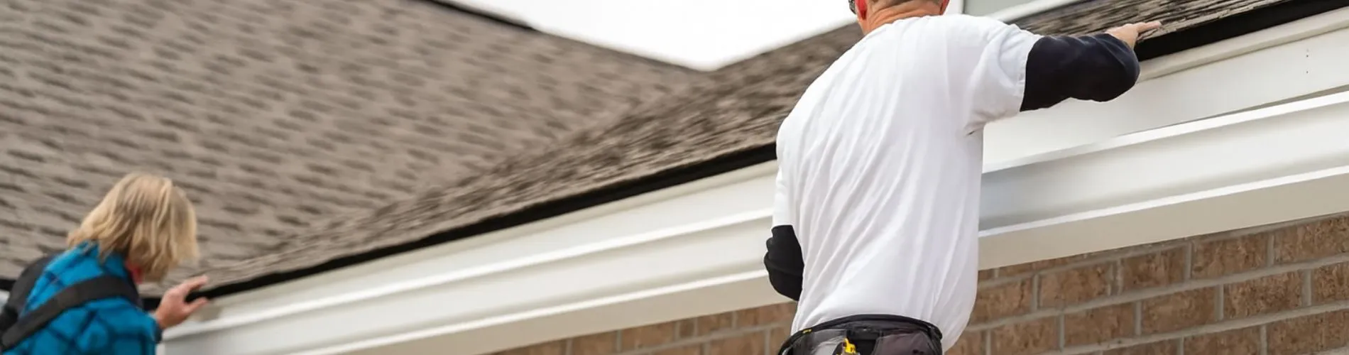Gutter installer working along a white gutter at the roofline of a brick home